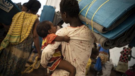 An Ethiopian refugee and her child collect mats at a transit site