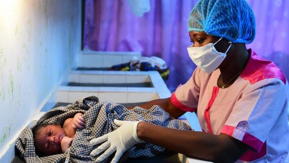 A nurse wearing a protective mask and gloves dresses up a newborn