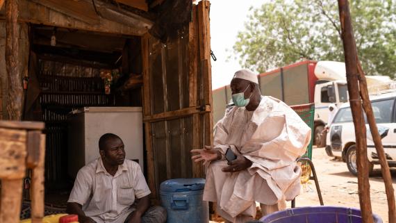 A community leader wearing a protective mask talks to a villager