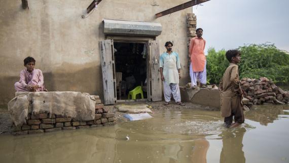 A group of young men stands outside their flooded home