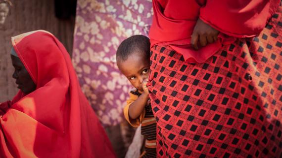 A boy hides behind a woman