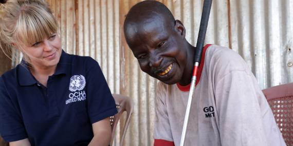 A blind men smiles next to a young humanitarian worker