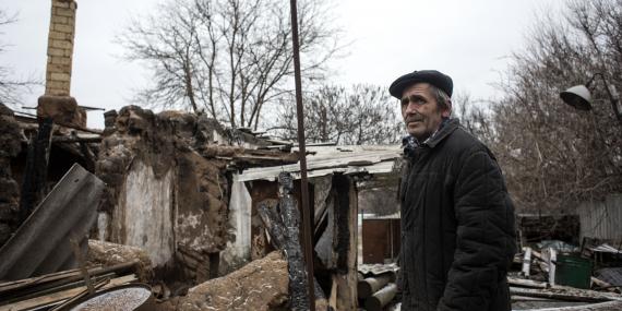 An old man in front of a destroyed house